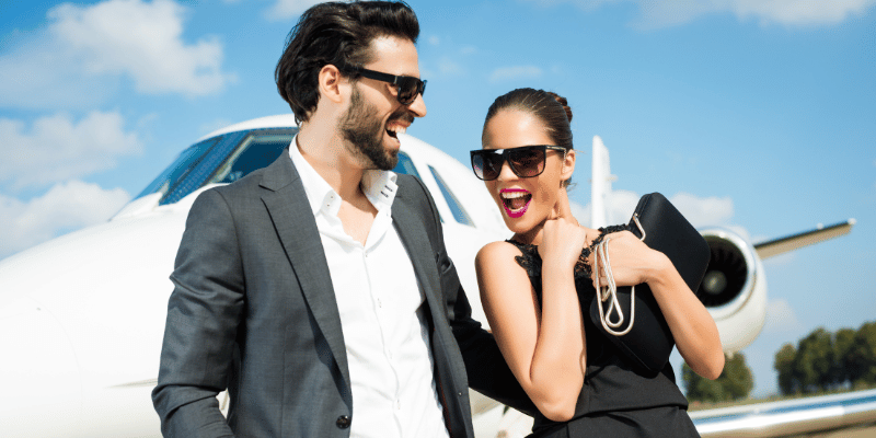 Rich people laughing in front of a plane.